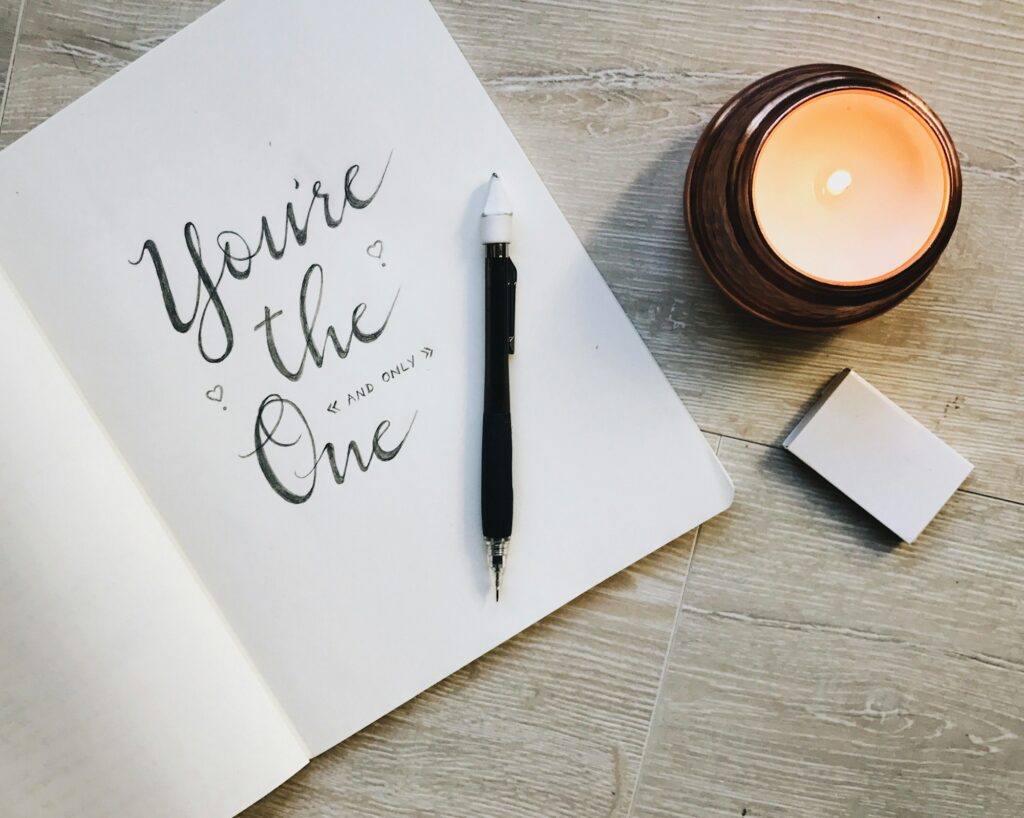 Calligraphy and scripted writing in a notebook with a mechanical pencil and candle with matches.